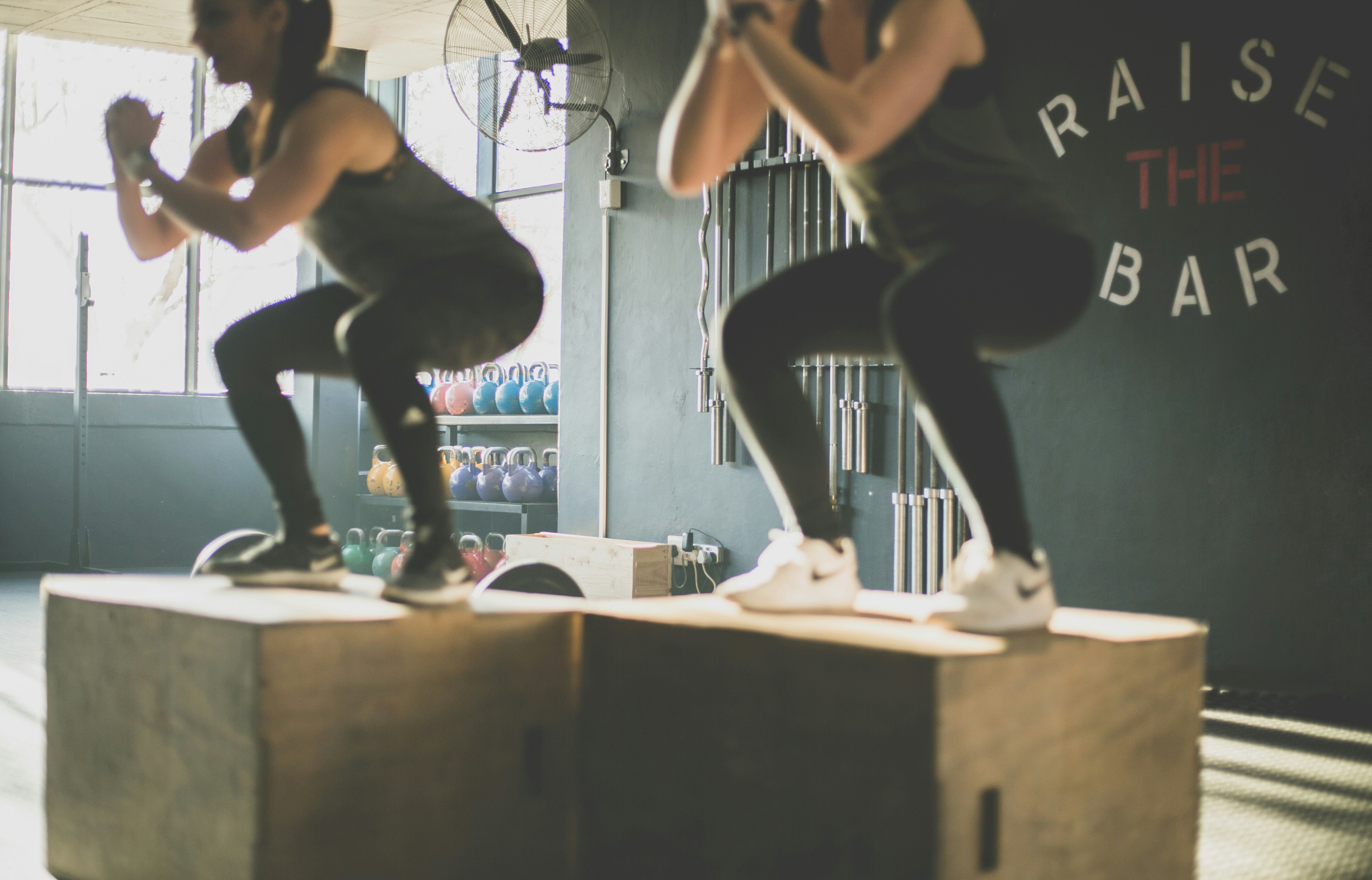 Two women doing box jumps in a CrossFit gym with Raise the Bar on the wall