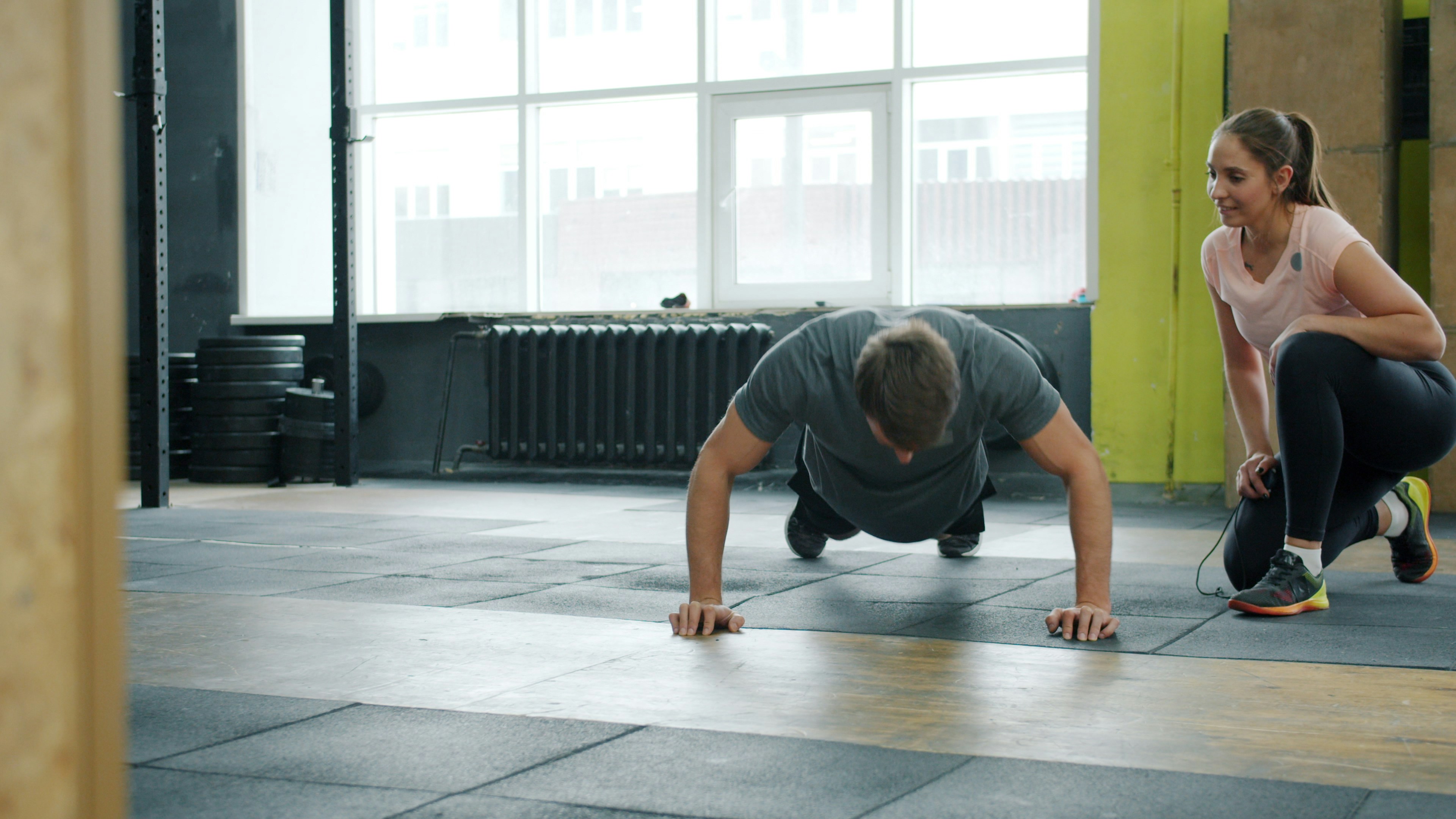 Trainer guiding a client through push-ups in a bright gym